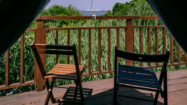 Een tentenveld met een houten terras, twee banken en uitzicht op zee.