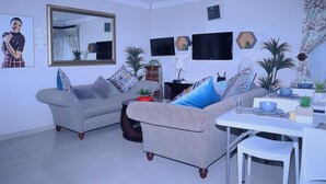 A living room with two grey sofas, a coffee table, and a dining area with a white table and chairs.