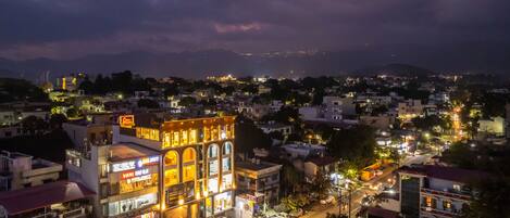 A multi-story building with illuminated signage, a street in the foreground, and a mountainous backdrop.