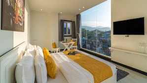 Une chambre d’hôtel équipée d’un lit, d’un bureau, d’une chaise, d’une télévision et d’une grande fenêtre donnant sur la ville.