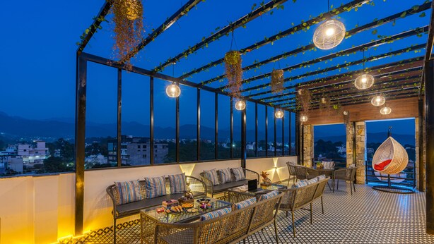 Une terrasse sur le toit, dotée d’un sol à motifs, d’un espace salon avec des coussins, de guirlandes lumineuses et offrant une vue sur le paysage urbain.