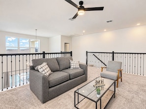 A modern living room with a grey sofa, a wooden chair, a glass coffee table, and a black railing. - Sunny Escape/ Private Pool, Jacuzzi & Waterpark (Davenport)