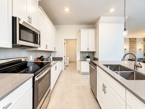 Una cocina moderna con electrodomésticos de acero inoxidable, armarios blancos y una isla central con un lavamanos.