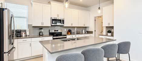 A modern kitchen with white cabinets, stainless steel appliances, a central island with bar stools, and pendant lighting.