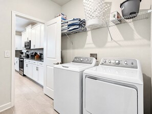 A laundry area with two front-loading washing machines, a drying rack with folded towels, and a microwave above a countertop.