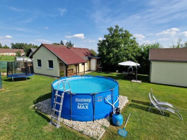Un jardin avec une piscine hors sol bleue, un trampoline et un espace patio couvert.