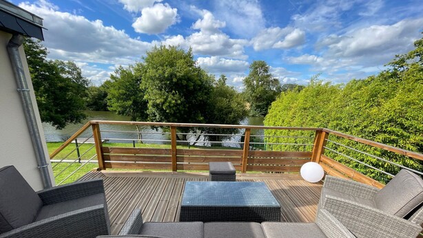 A covered outdoor deck with wicker furniture and a view of a lake.