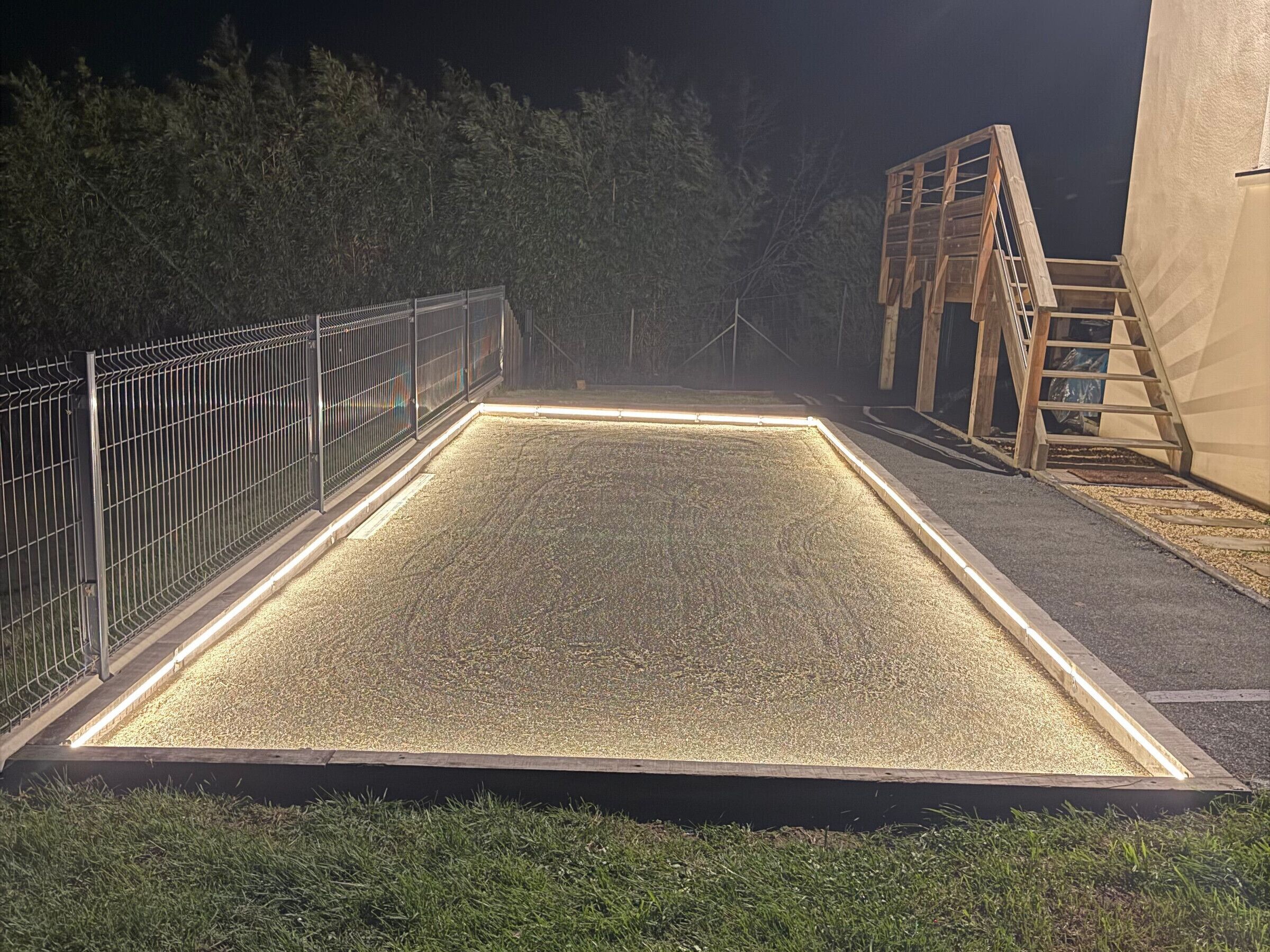 A rectangular outdoor area with a metal fence, a wooden structure, and a gravel surface.