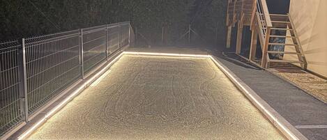 A rectangular outdoor area with a metal fence, a wooden structure, and a gravel surface.
