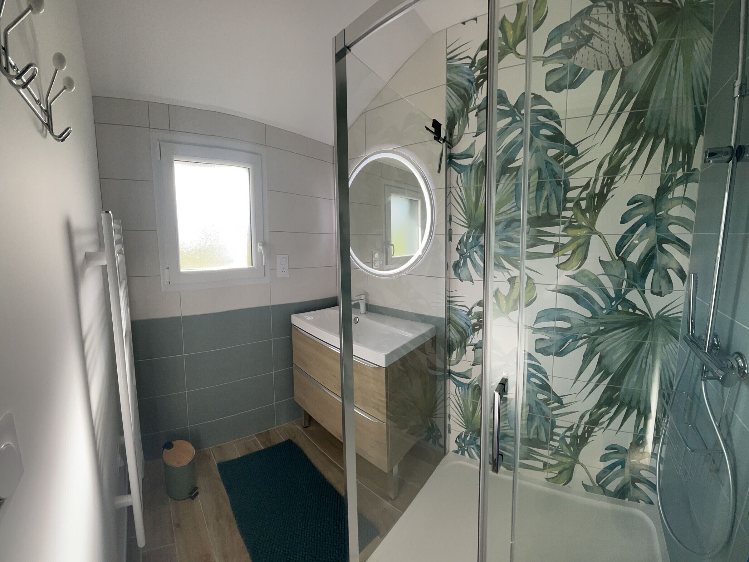 Une salle de bain moderne avec une douche à l’italienne en verre, un lavabo avec un miroir et une fenêtre.