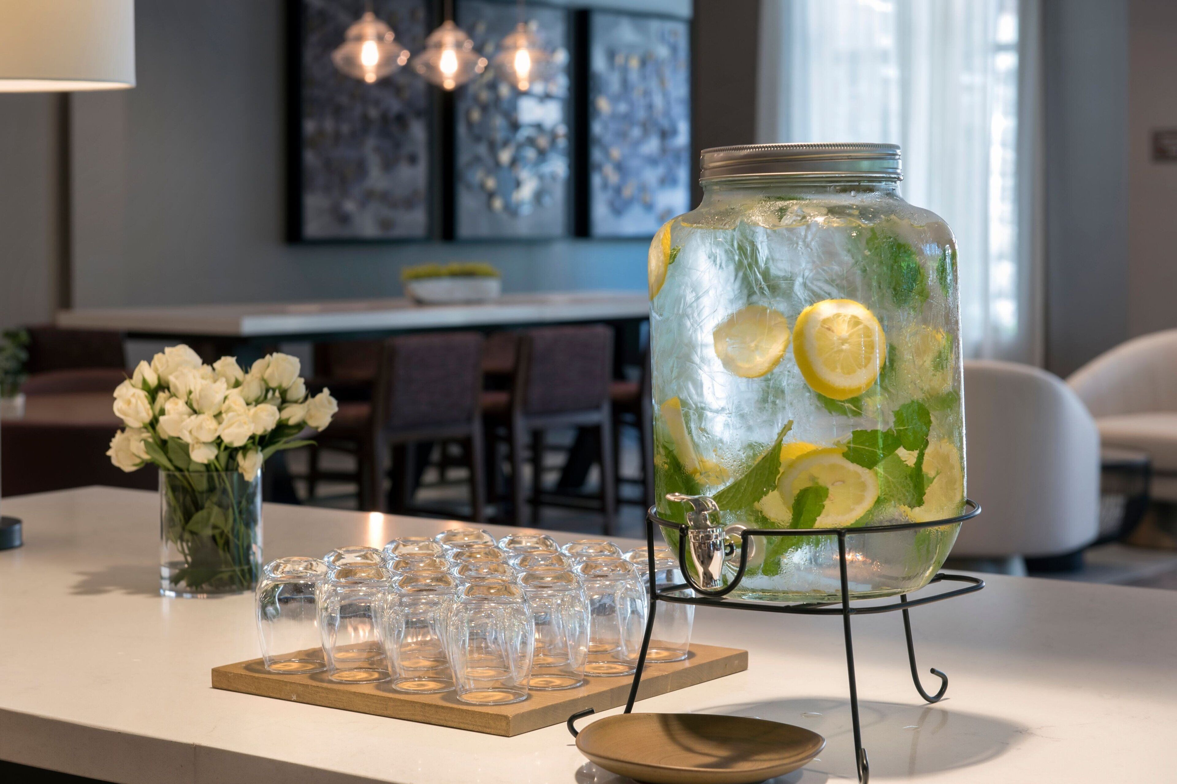 En køkkenbordplade med et stort glas med drikke, omgivet af tomme glas og en skål.