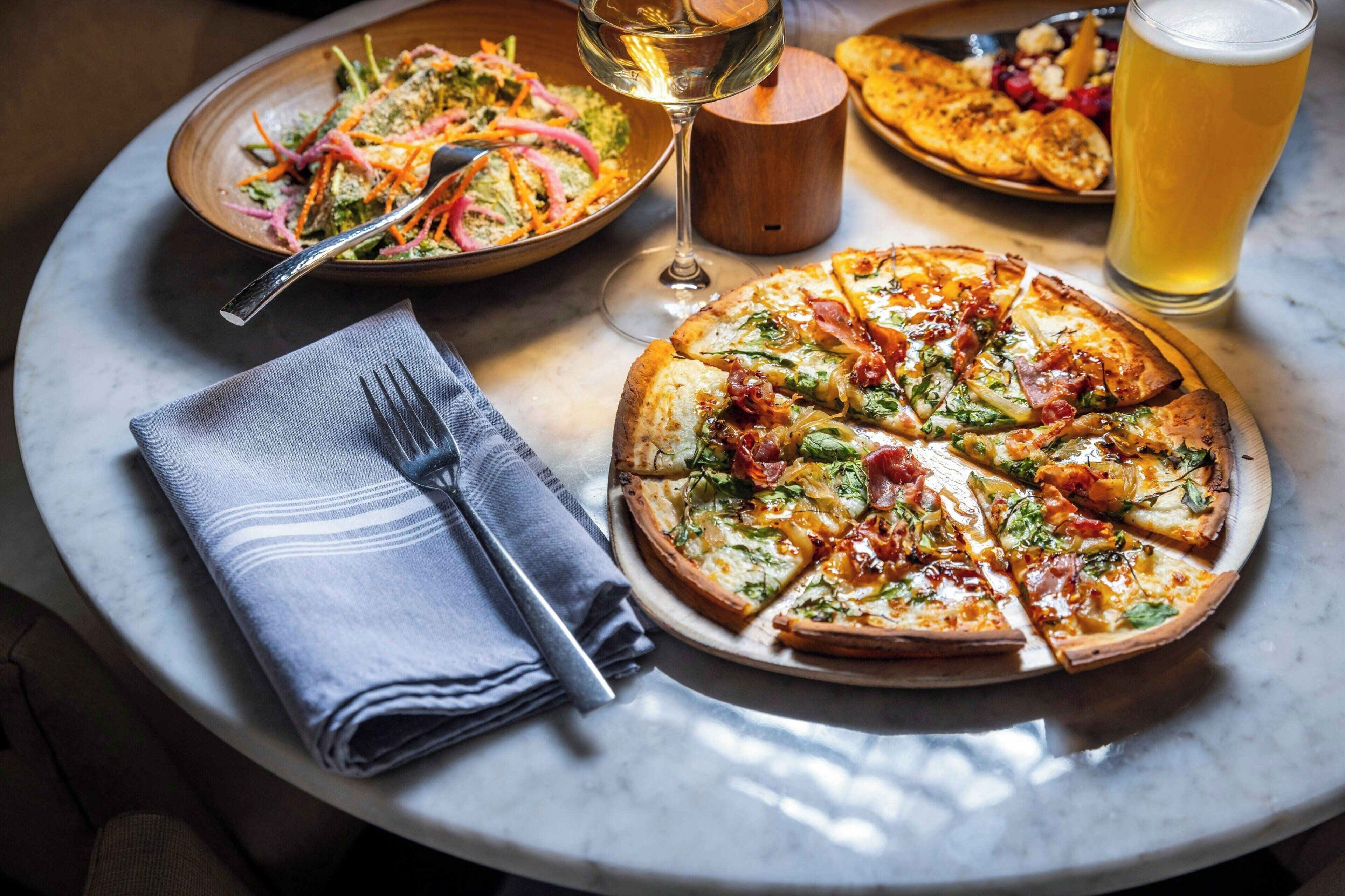 Ett runt bord med en pizza, en sallad, ett glas öl och ett vinglas.