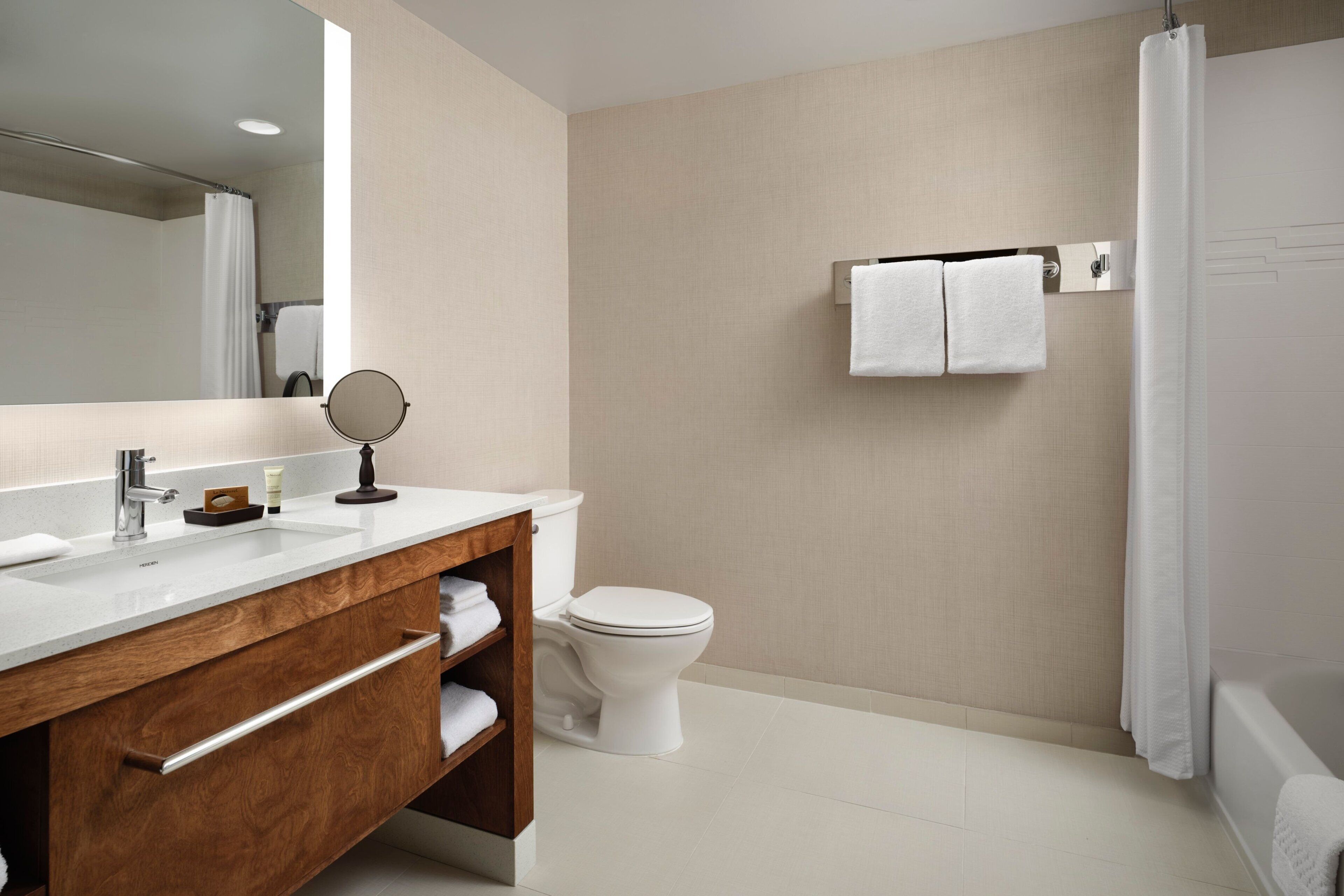 A modern bathroom with a wooden vanity, a round mirror, a toilet, and a bathtub.