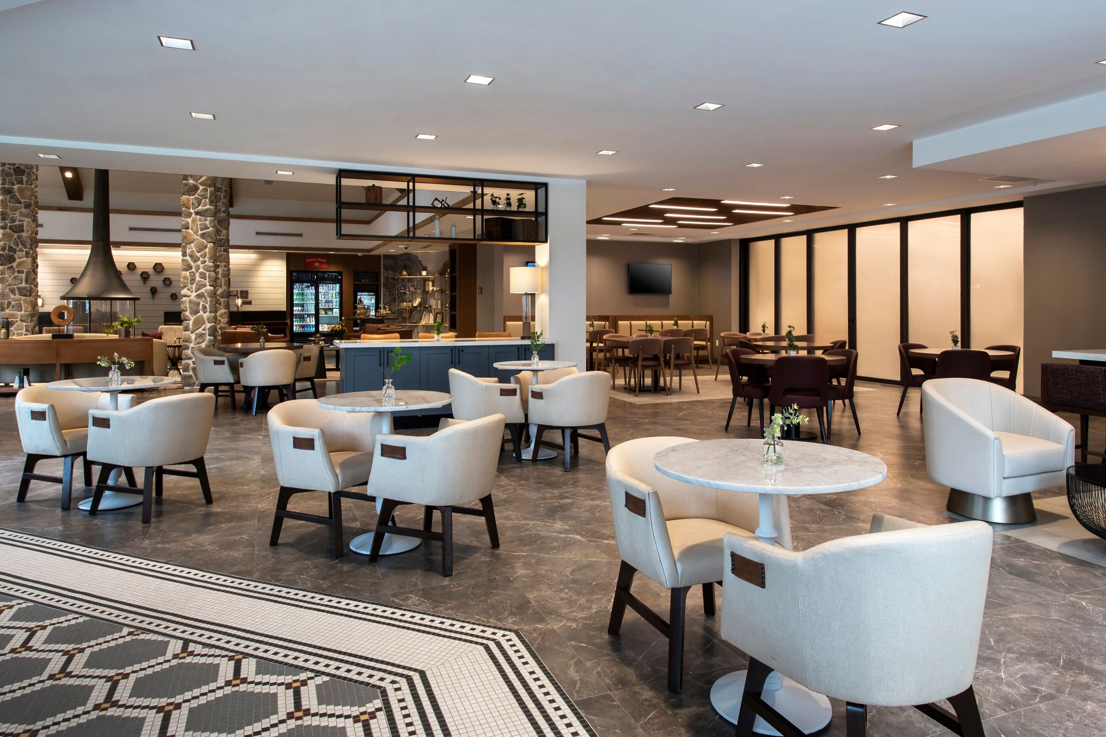 Un moderno vestíbulo de hotel con mesas redondas, sillas acolchadas, una zona de bar y una alfombra estampada.