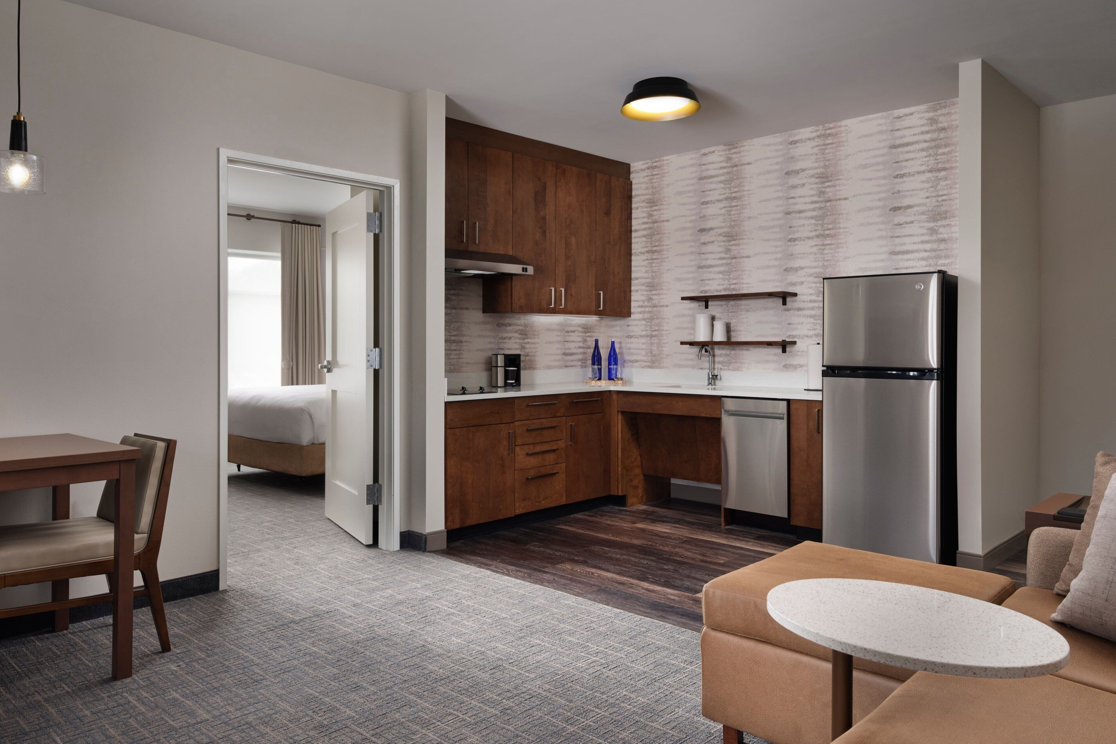 A modern kitchen with wooden cabinets, a stainless steel refrigerator, and a small dining area with a table and chairs.
