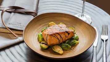 Ein Teller gegrillter Lachs mit Rosenkohl auf einer strukturierten Platte, dazu ein Glas Weißwein und eine gefaltete Speisekarte.