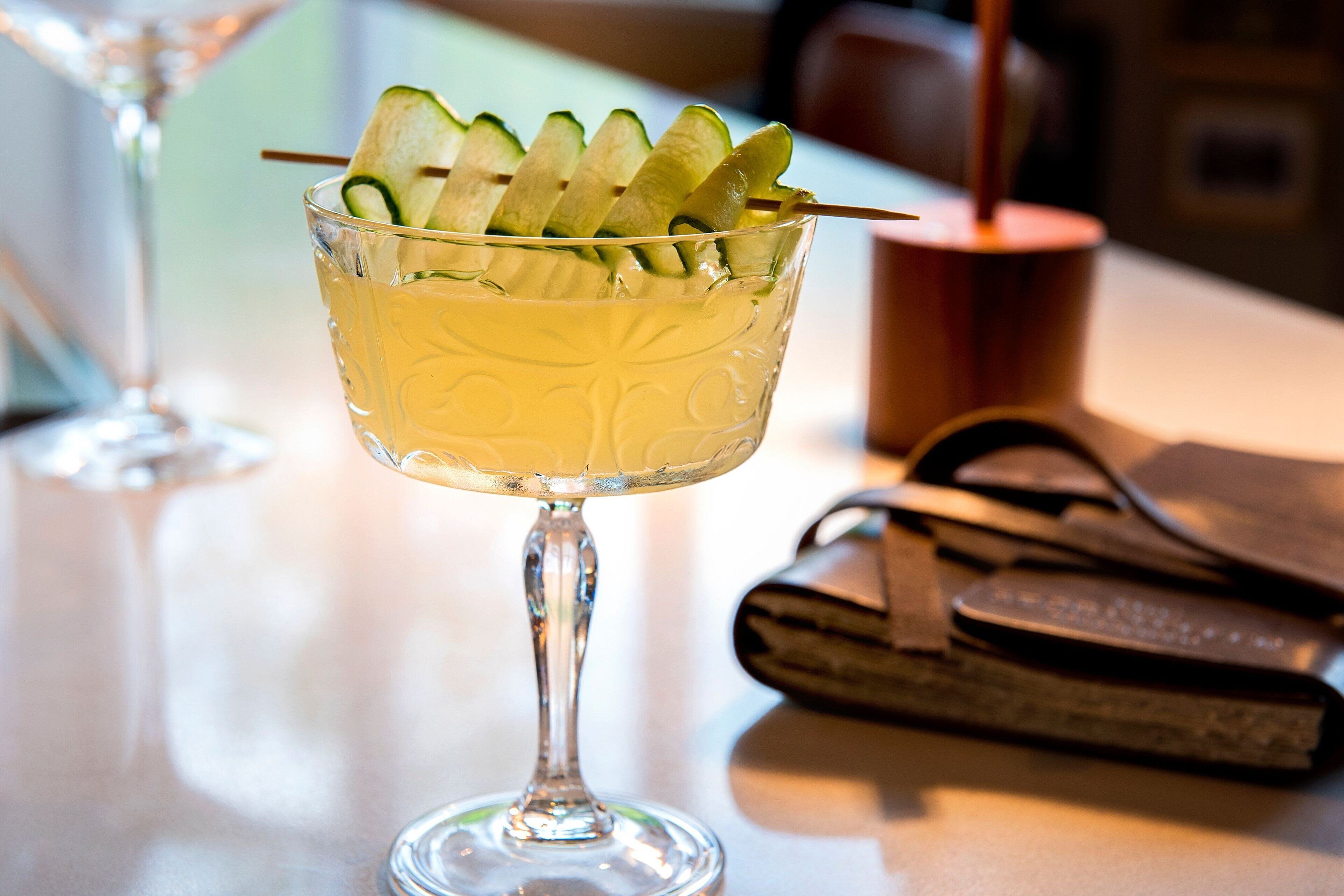 A cocktail glass with cucumber slices on a bar counter.