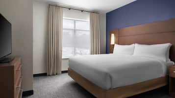 A hotel room with a bed, a TV, a nightstand, a lamp, and a window with curtains.