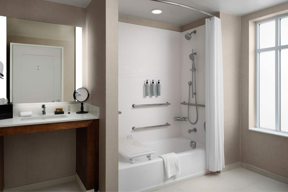 Une salle de bain moderne équipée d’une douche, d’un meuble-lavabo avec miroir et d’une fenêtre laissant entrer la lumière naturelle.
