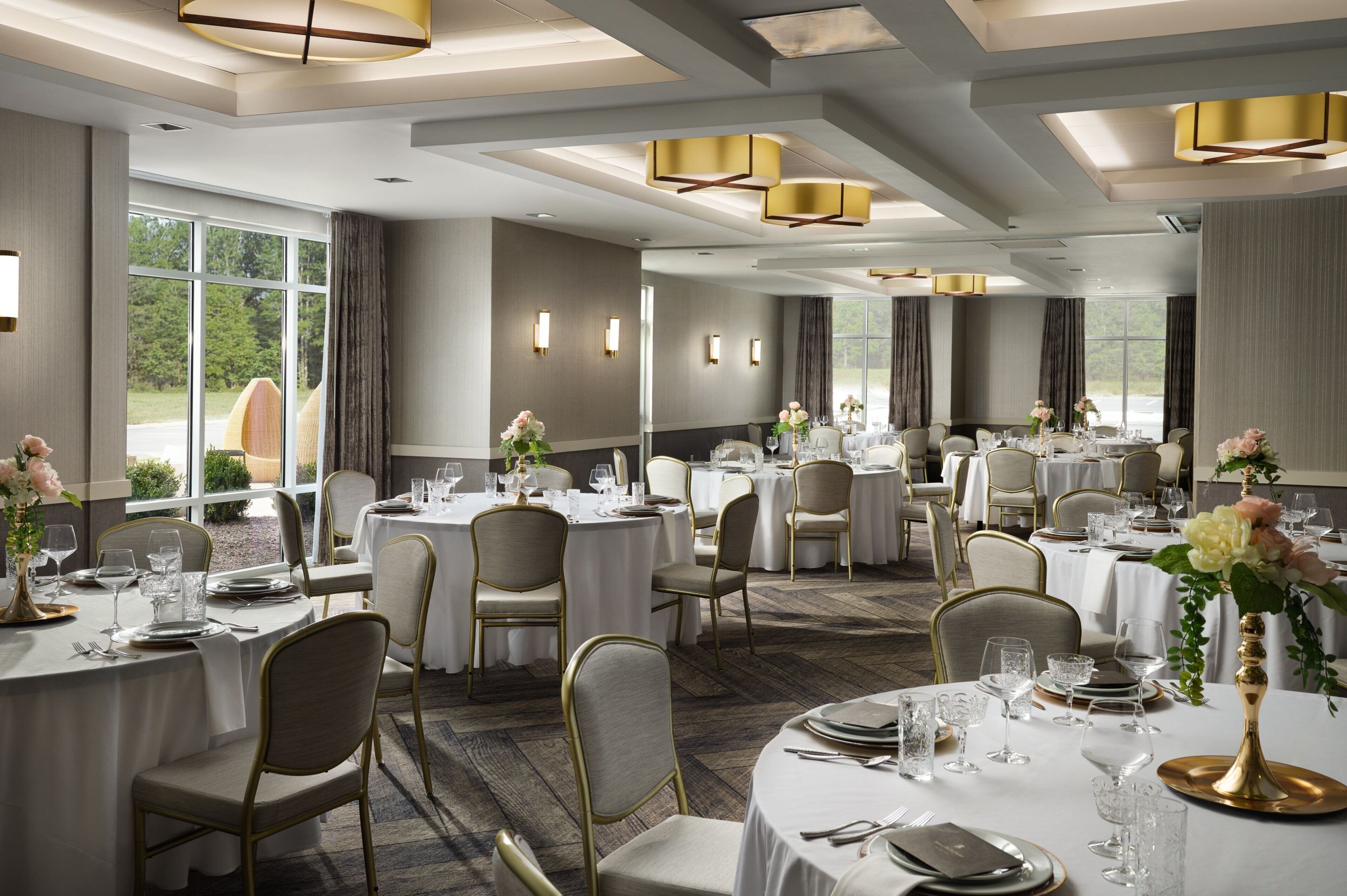 A spacious dining area with round tables, chairs, and chandeliers.
