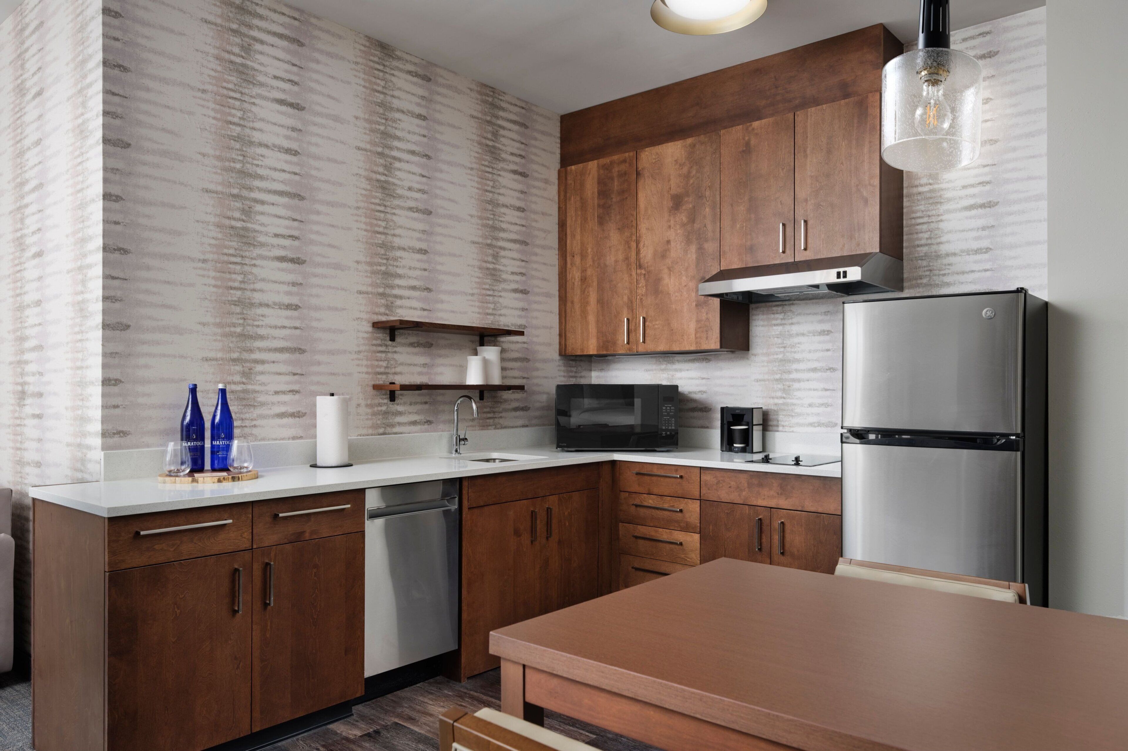 A modern kitchen with wooden cabinets, a stainless steel refrigerator, a microwave, and a coffee maker.