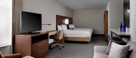 A hotel room with a bed, a desk with a chair, a television, a sofa, and a mirror.