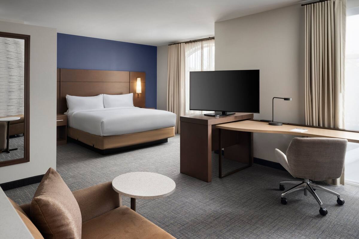 Une chambre d’hôtel avec un lit, un bureau, une chaise, une télévision et une petite table.