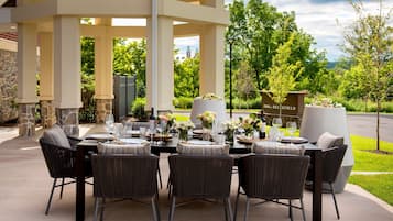 Un espace de restauration en plein air doté d’un patio couvert, de piliers en pierre et offrant une vue sur la végétation et les collines environnantes.