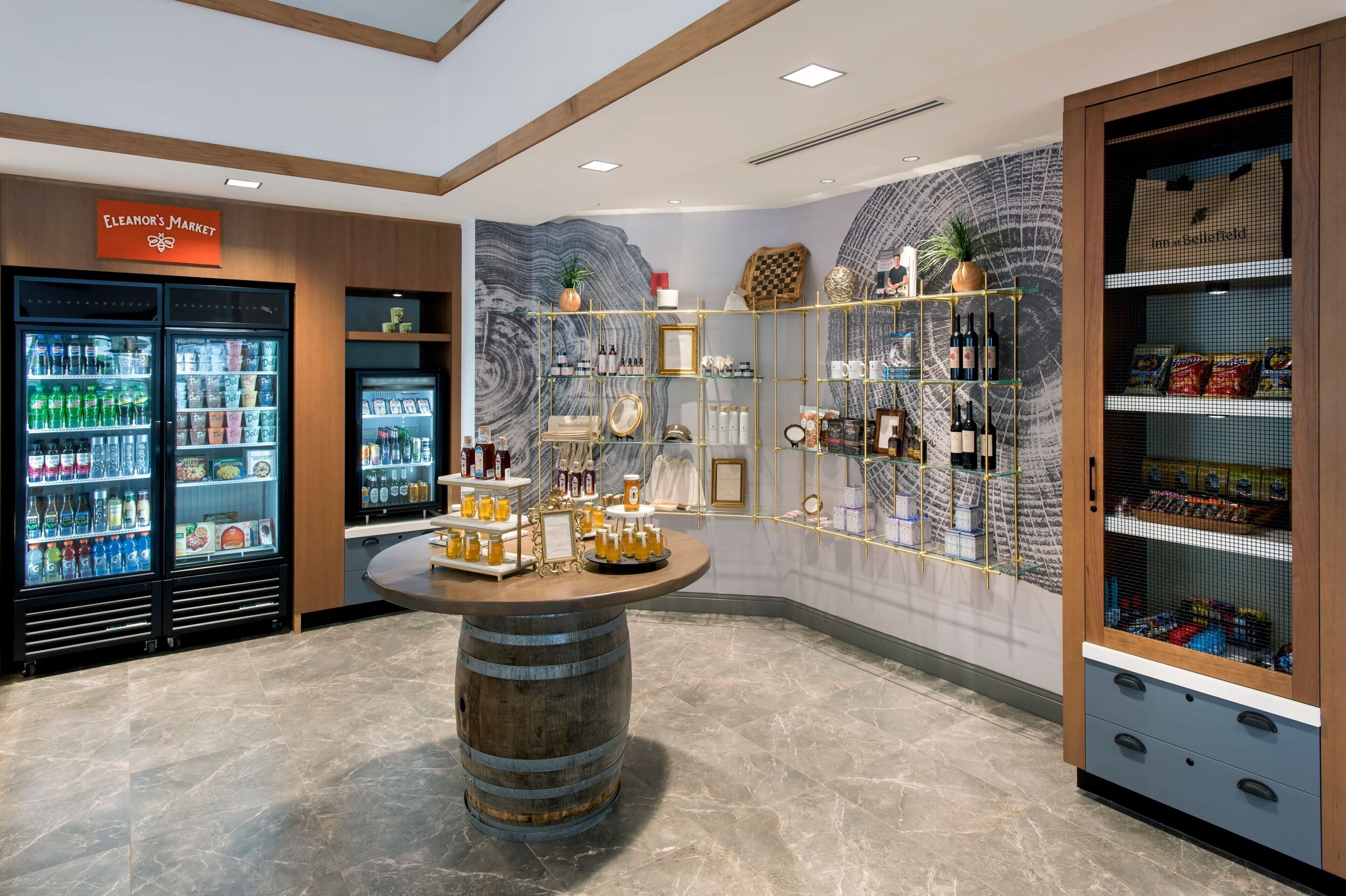 A well-lit retail space with a central round table displaying various items, surrounded by shelves stocked with products and a backdrop of a textured wall.