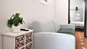En moderne stue med en grå sofa, et hvidt skab med dekorative fliser, en potteplante og et kunstværk på væggen.