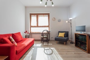 A living room with a red sofa, a grey armchair, a wooden floor, a window with curtains, a floor lamp, and a TV on a wooden cabinet. - Saluzzo House by Wonderful Italy (Turin)