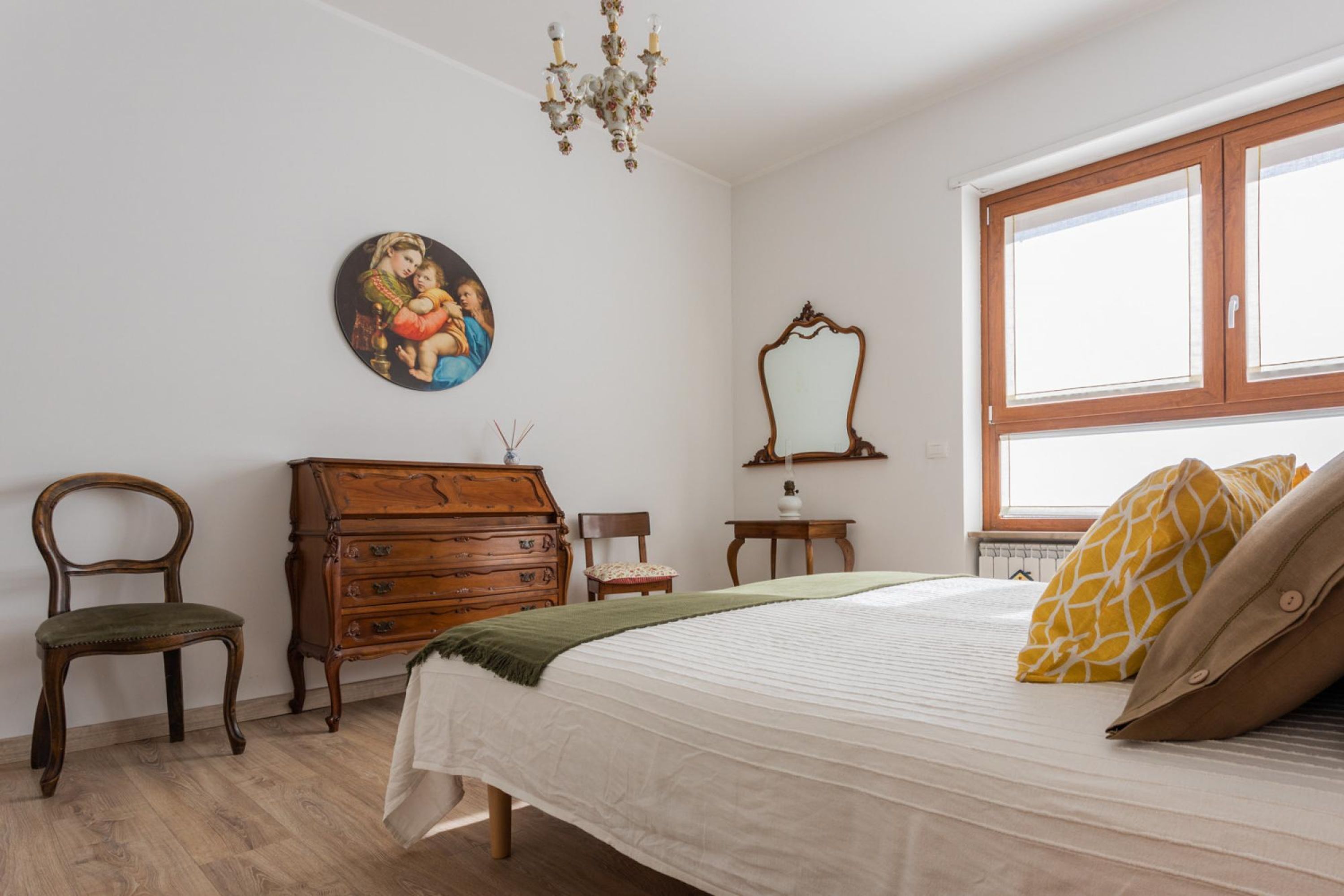 A bedroom with a bed, wooden dresser, chair, and a painting on the wall.