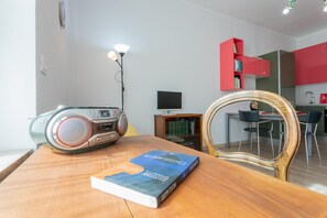 A modern living room with a wooden table, a book titled 'E. Success Story: The Art of Self-Improvement', a radio, and a dining area with a red cabinet and a TV. - Saluzzo House by Wonderful Italy (Turin)