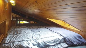 Un dormitorio con techo inclinado, paredes de madera, una cama con manta estampada y un ventanal pequeño.