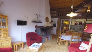 Una sala de estar acogedora con chimenea, sillones rojos, una mesa de centro de madera y un comedor con mesa y sillas.