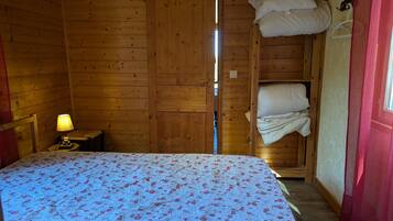 A wooden cabin room with a bed, a nightstand, and a window.