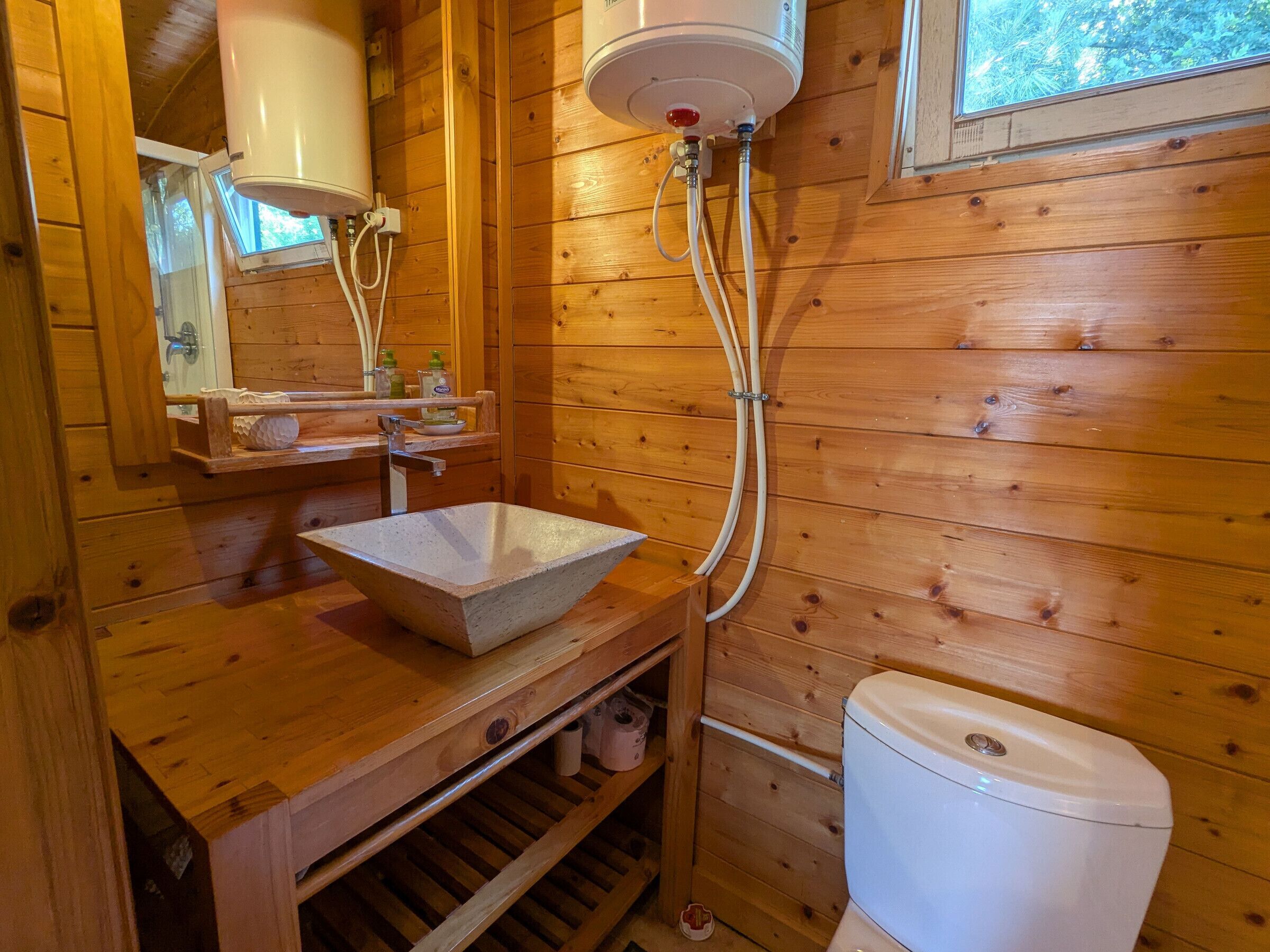 Een houten badkamer met een stenen wastafel, toilet en raam.