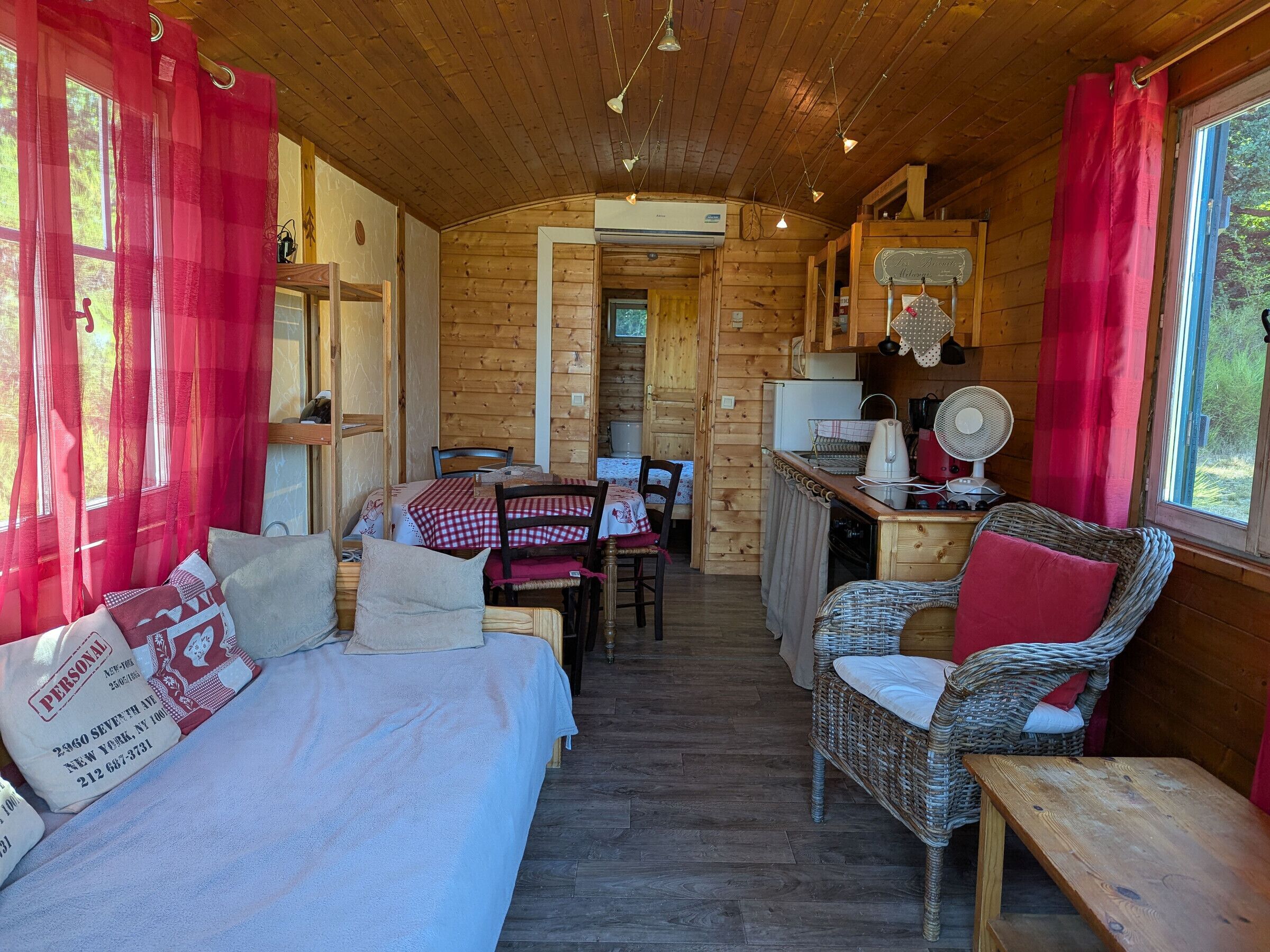 Een gezellig chaletinterieur met een bed, een eettafel, rieten stoelen, een keukenhoek en uitzicht door een raam.