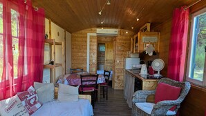 A cozy cabin interior with a bed, dining table, wicker chairs, a kitchen area, and a view through a window. - Charming 28m² Gypsy Caravan in Val de Loire, Sleeps 4, Near Castles & Bike Trails (Lion-en-Sullias)