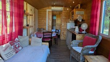 Een gezellig chaletinterieur met een bed, een eettafel, rieten stoelen, een keukenhoek en uitzicht door een raam.