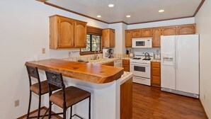 A kitchen with wooden cabinets, a white refrigerator, a stove, and a bar area with stools.