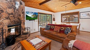 A cozy living room with a stone wall, a fireplace, a leather sofa, and a television mounted on the wall.