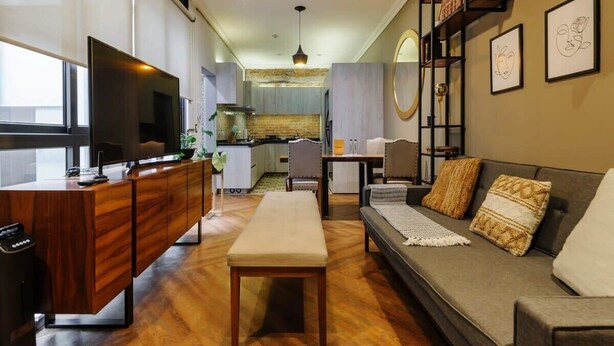 A modern living room with a wooden coffee table, a grey sofa with patterned cushions, a flat-screen TV, and a kitchen in the background. - w* | Stylish 2BR in Cuauhtemoc (Ciudad de México)