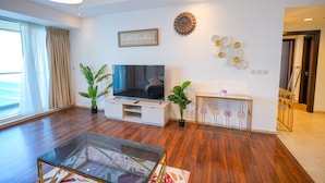 Un salon moderne doté d’un téléviseur à écran plat, de parquet, d’une table basse en verre et d’une console sur laquelle sont disposés des objets décoratifs.