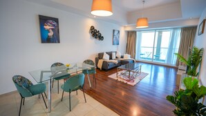 Un salon moderne avec une table à manger en verre, des chaises turquoise, un canapé gris et une grande fenêtre avec des rideaux.