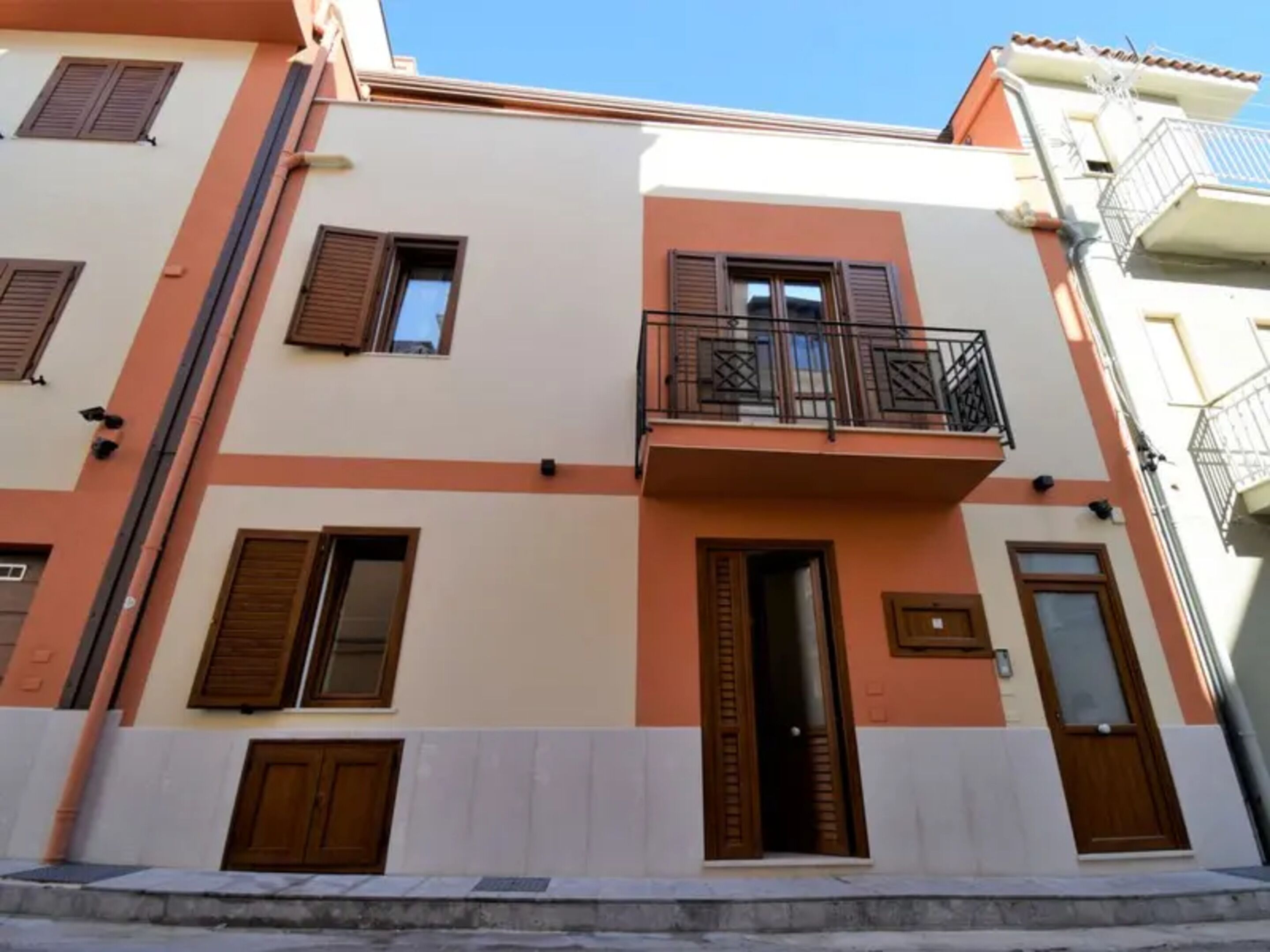 A multi-story building with a balcony on the second floor, a door on the ground floor, and a window on the first floor.