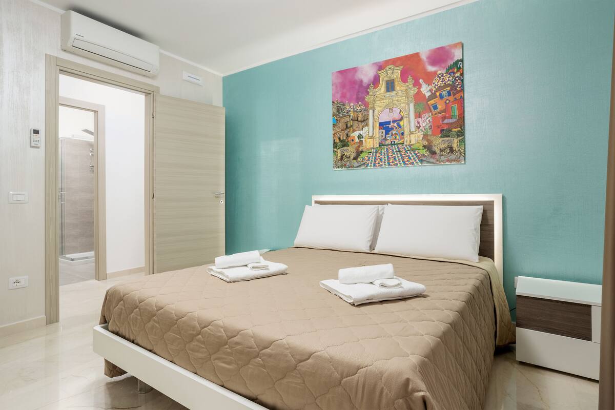 A bedroom with a bed, a painting on the wall, and a door.