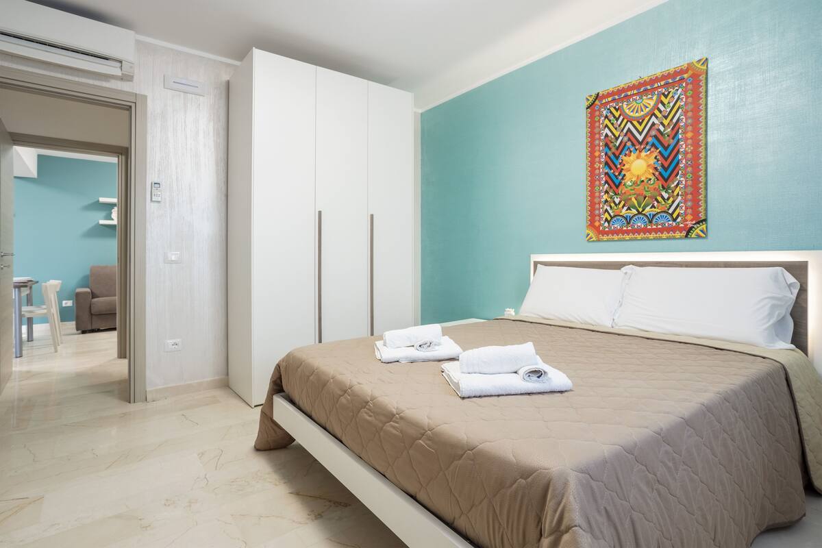 A hotel room with a bed, a wardrobe, a bathroom, and a view of the outside.