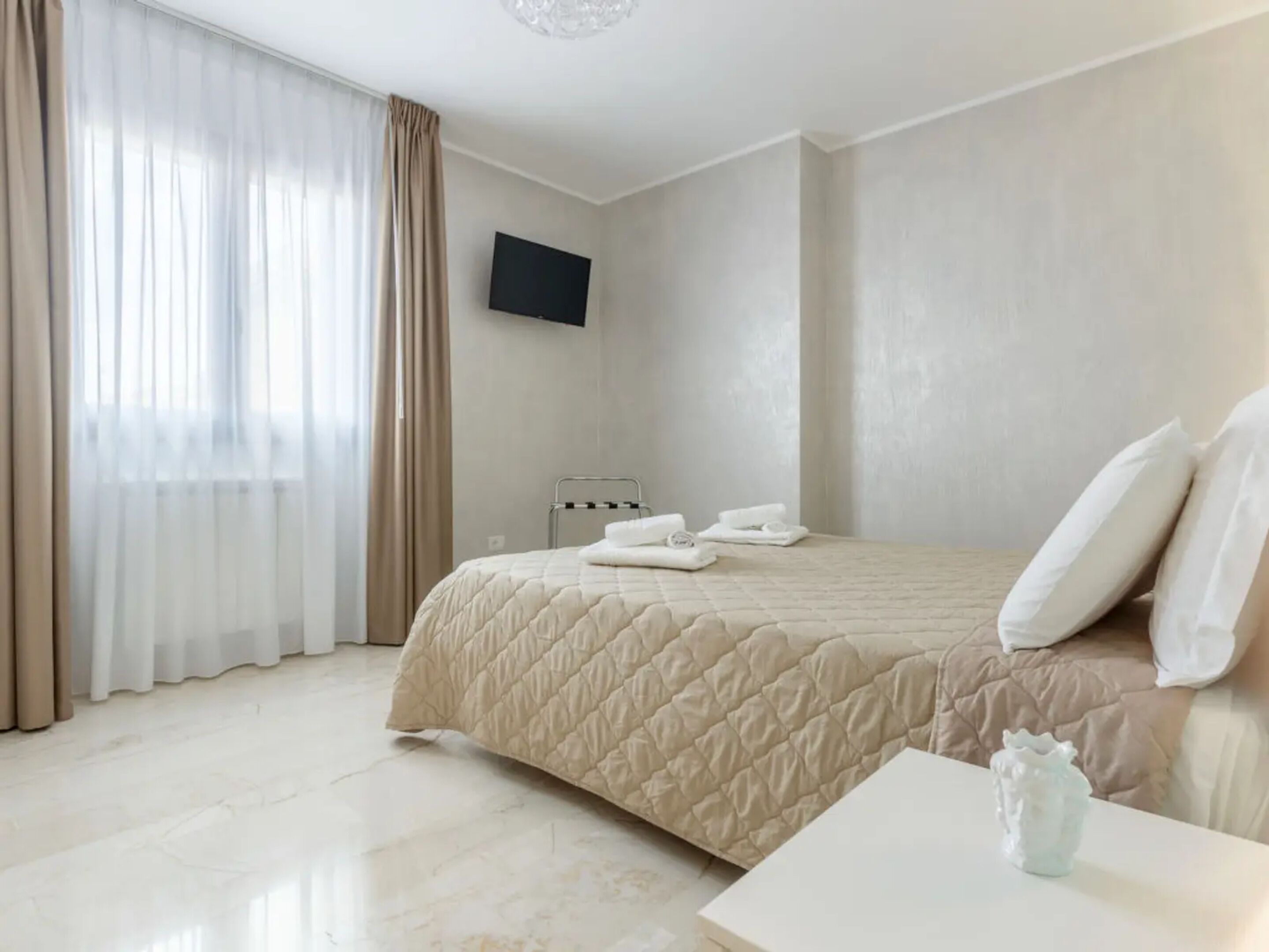 Habitación de hotel con cama, televisión de pantalla plana, mesita de noche y ventana con cortinas.