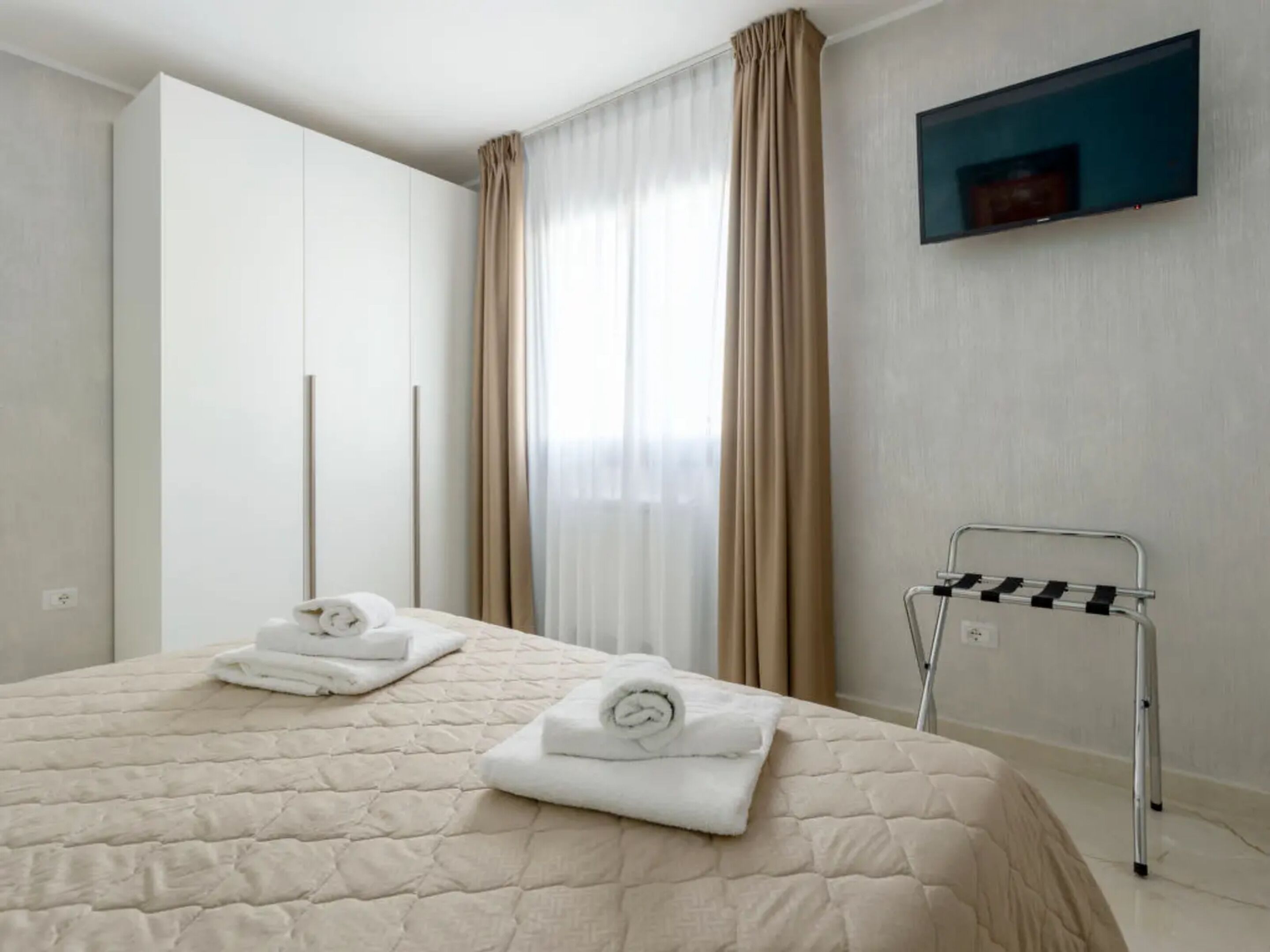 A hotel room with a bed, a TV mounted on the wall, and a towel rack.